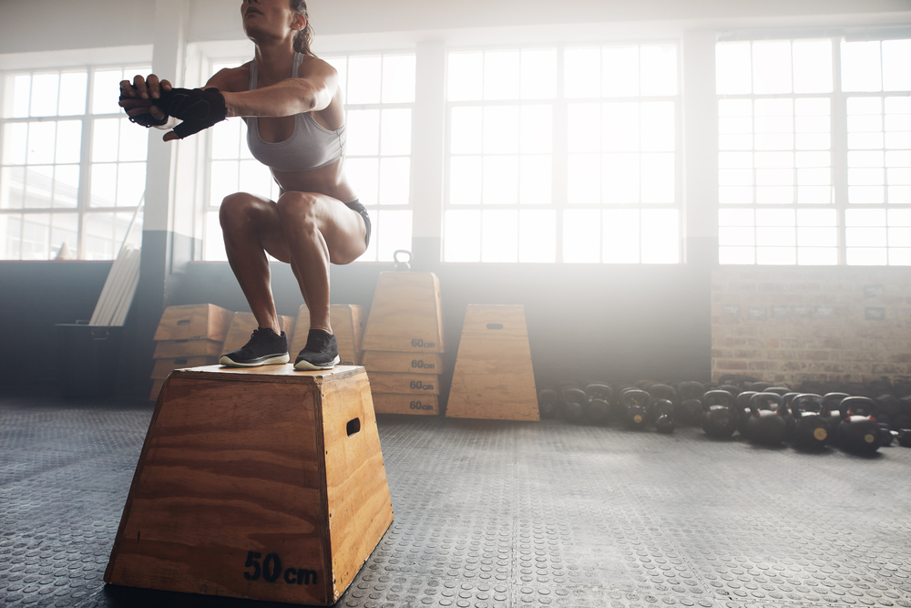 Shot of a young woman jumping onto a box as part of exercise routine.